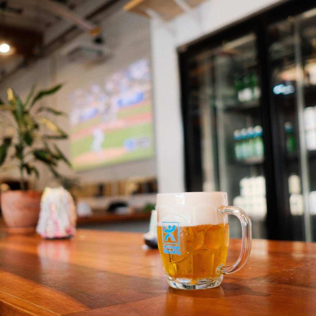 glass of beer on the bar at Homage Brewing’s Chinatown location in Downtown Los Angeles, with a baseball game on in the background.