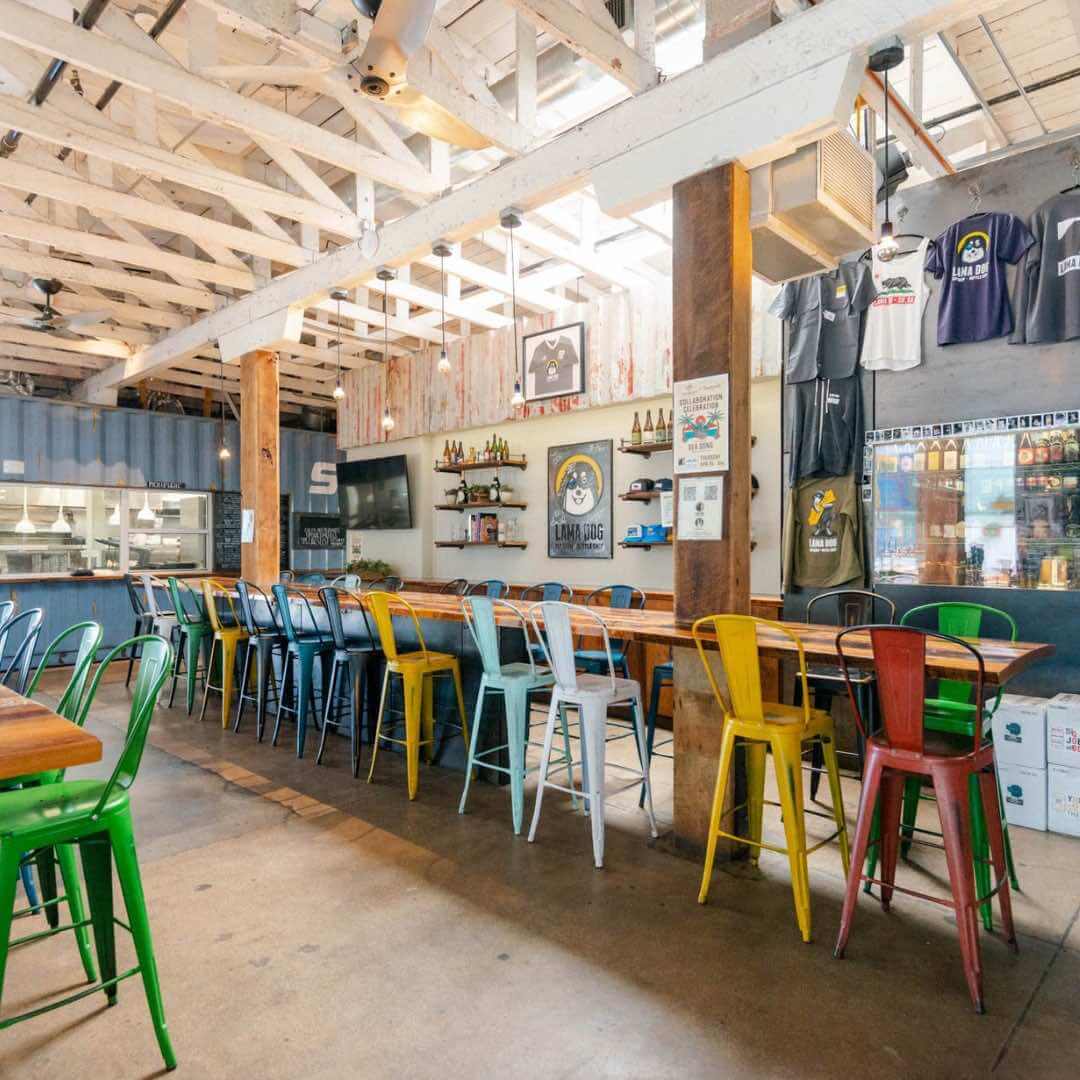Interior of Lama Dog Tap Room + Bottle Shop in Santa Barbara’s Funk Zone, with colorful chairs and rustic decor.