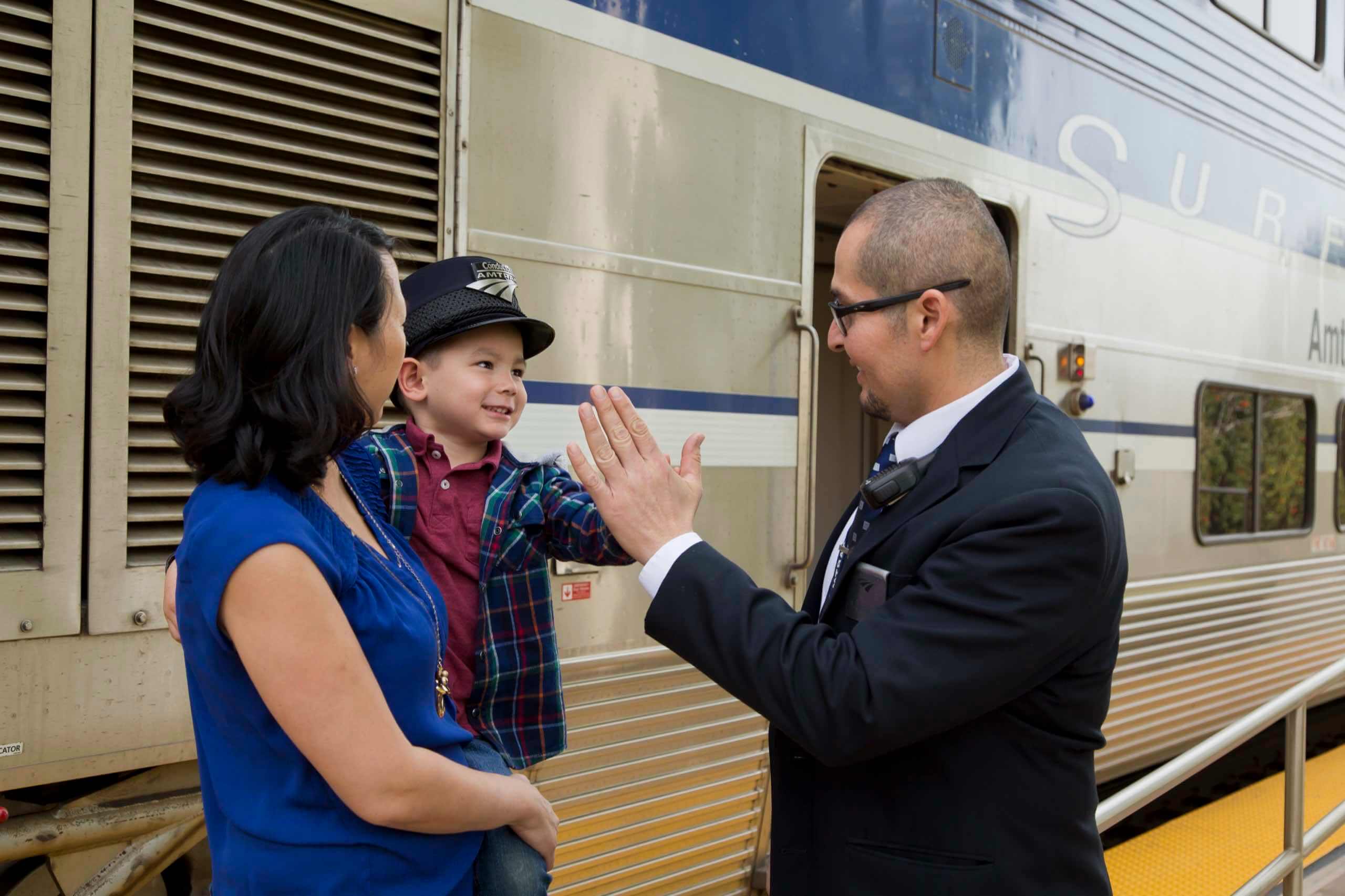 A young boy wearing an Amtrak conductor hat gets a high five from a Pacific Surfliner crew member.
