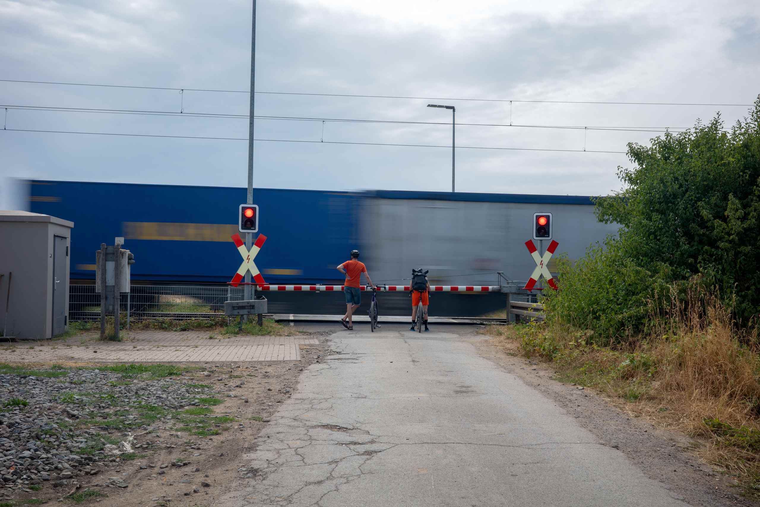 Two cyclists wait at a railroad crossing while a train passes.