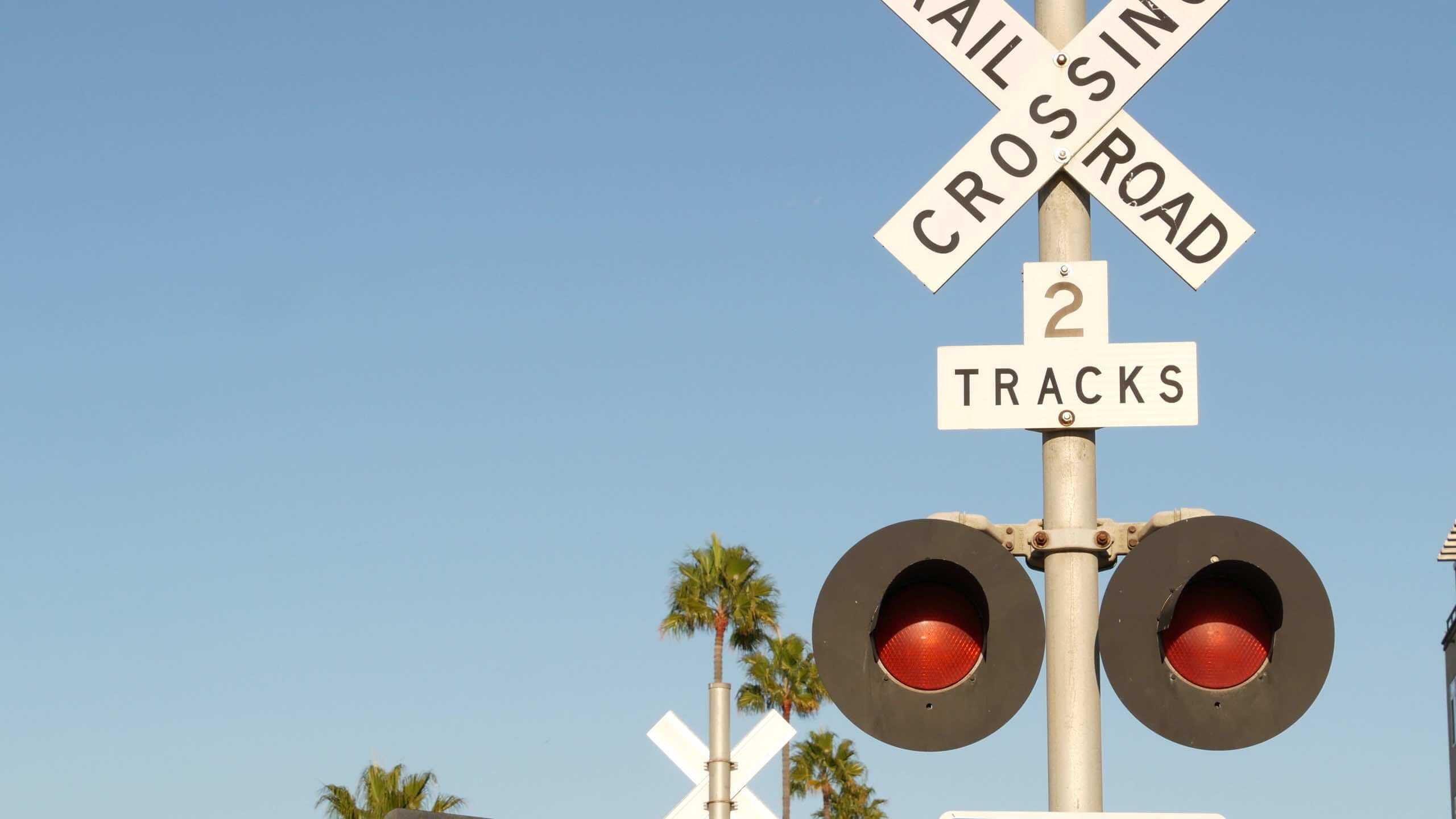 Railroad crossing safety signals and a "2 Tracks" crossing sign beneath a clear blue sky.