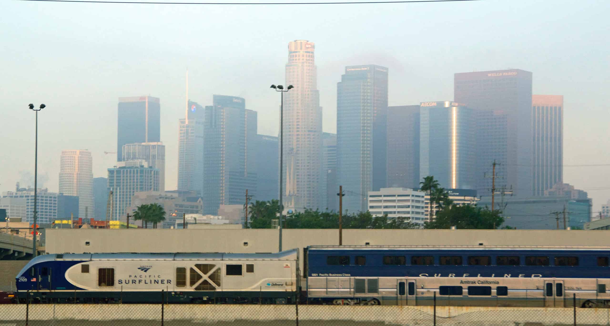 Pacific Surfliner train traveling through Los Angeles with the downtown LA skyline in the background.